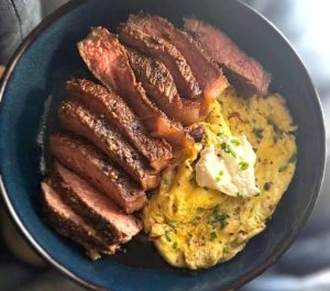 A vibrant breakfast bowl with sliced hanger steak, a poached egg, and green chimichurri sauce.