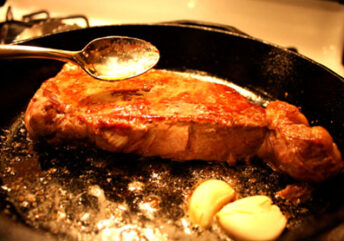 A sizzling piece of grass-fed beef frying in rich, melting butter in a hot pan, symbolizing the delicious and potent beef and butter benefits for energy and nutrition.