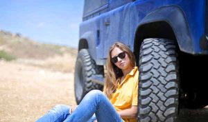 Losing weight on the steak and eggs diet featuring a girl sitting near the front wheel of a blue jeep in a yellow t shirt and jenese trouser.