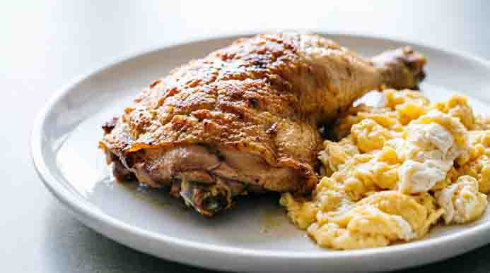 Single roasted chicken thigh quarter topped with a melting pat of butter in a shallow earth-toned ceramic bowl.