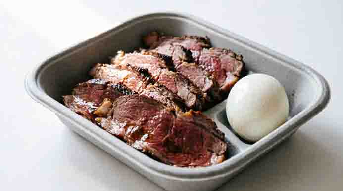 Sliced medium-rare roast beef and a whole peeled hard-boiled egg packed in a sustainable fiber lunch container.