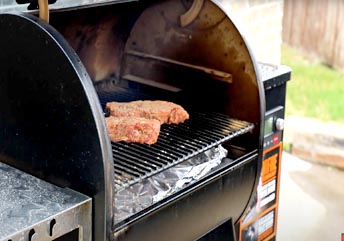 A thick ribeye steak being reverse seared on a Traeger pellet grill, showing smoke and a dark crust.