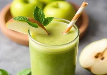 Vibrant green apple detox smoothie with spinach, ginger, and cucumber in a clear glass.