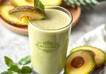 Creamy avocado and pineapple smoothie in a glass with mint garnish.