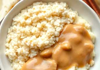 Close-up of a warm bowl of creamy oatmeal mixed with soft mashed chicken and savory gravy, a braces-friendly meal that's easy to chew and nutrient-rich, served on a white plate with a spoon.