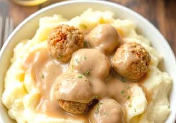 Close-up of a creamy mashed potato bowl topped with soft turkey meatballs and light gravy, a perfect braces-friendly meal, served with a spoon on a rustic table.