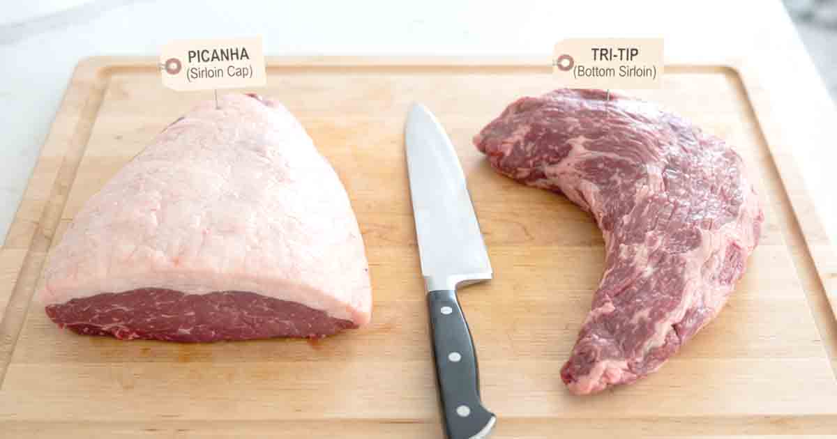 what is picanha, A side-by-side visual comparison of two raw beef cuts on a wooden cutting board: a picanha roast and a tri-tip roast. The picanha on the left displays its triangular shape and thick, even external fat cap, clearly labeled.