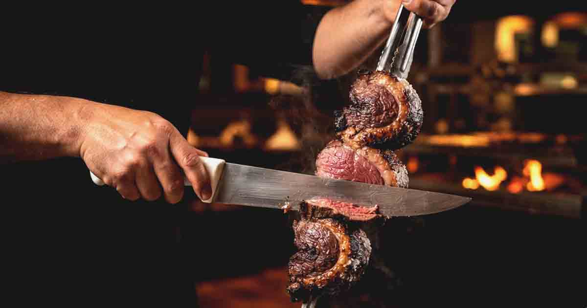 what is picanha, A gaucho chef's hands in a Brazilian steakhouse, using a sharp carving knife to slice a freshly grilled, salt-crusted picanha roast against the grain.