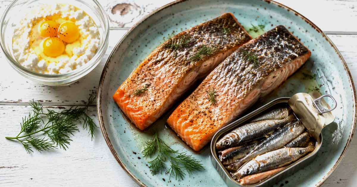 Pan-seared salmon fillets next to an open tin of sardines and dill garnish on a light blue plate.