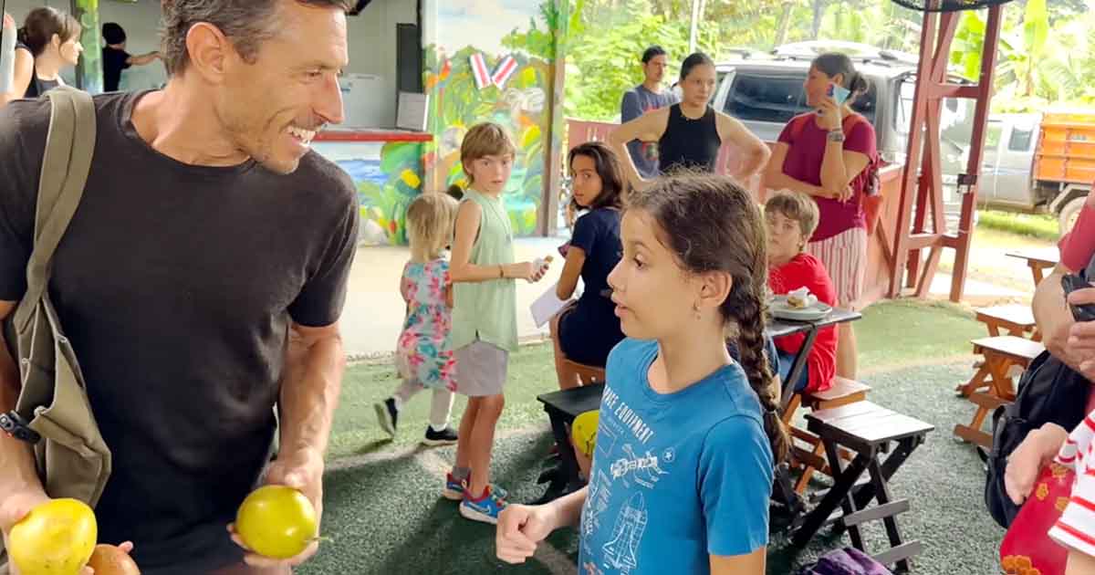 Dr. Paul Saladino (Carnivore MD) chatting warmly with a young girl at an outdoor local farm market while standing beside a fresh fruit display.