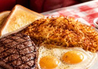 Perfect steak and eggs breakfast platter with ribeye, sunny-side-up eggs, and crispy hash browns on a wooden table.
